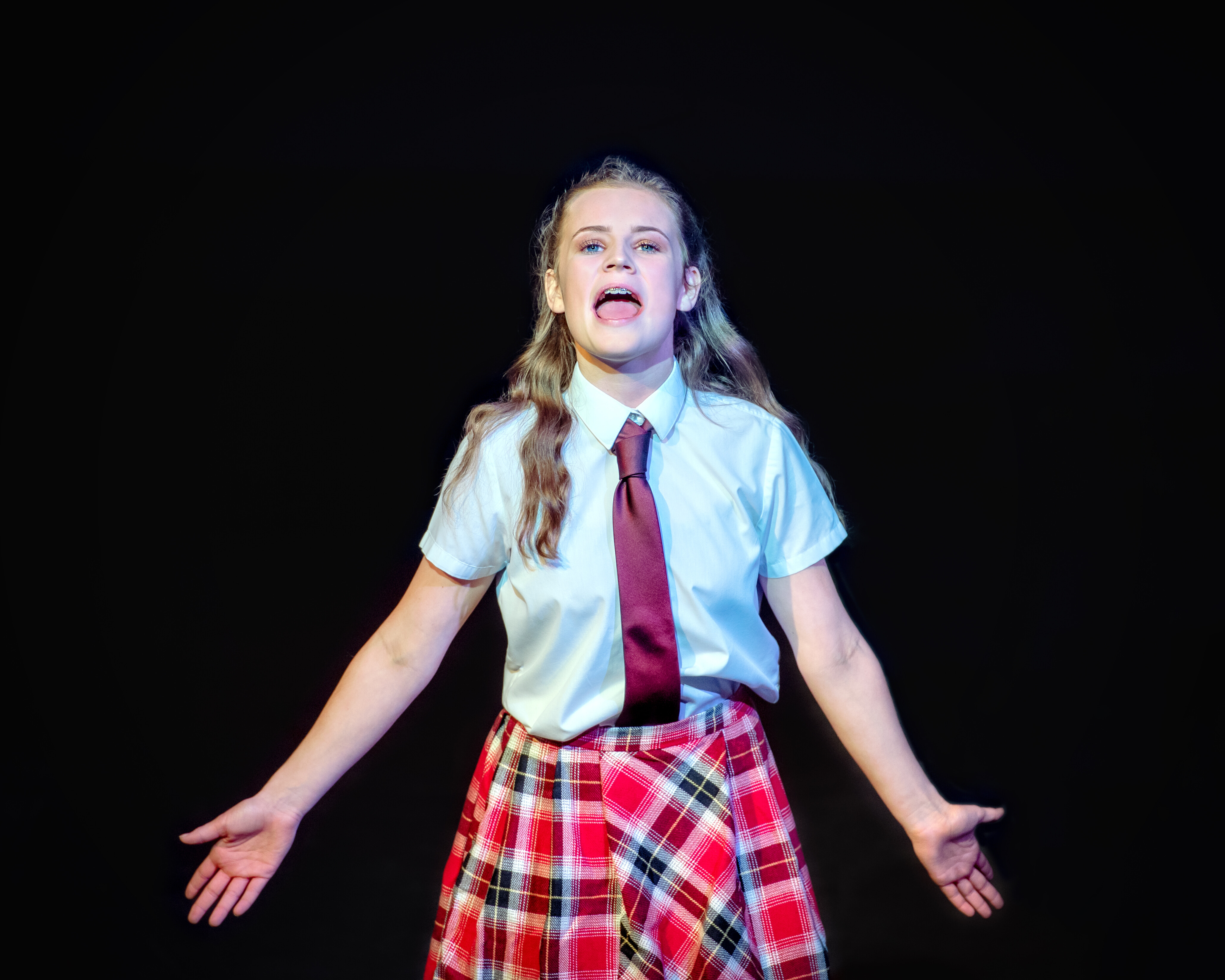 Image of performance academy student singing on stage, wearing a school uniform costume.