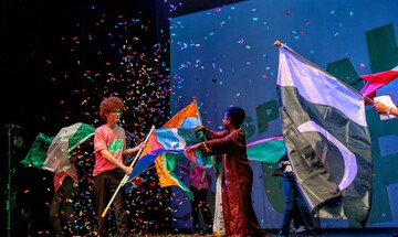 Young people onstage waving different national flags while confetti drops through the air