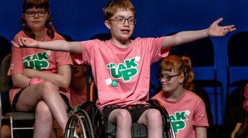 A student in a wheelchair centre stage, arms outstretched